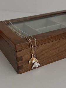 Detailed view of silver and gold fishtail pendants with pearls on a wooden jewelry box