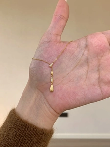 Dettaglio della collana a Y con gocce d'oro spazzolato, mostrata nel palmo della mano