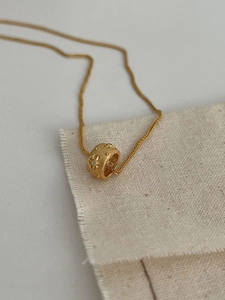 Detail view of a matte gold star-engraved cylinder pendant with micro zircons on a fine chain