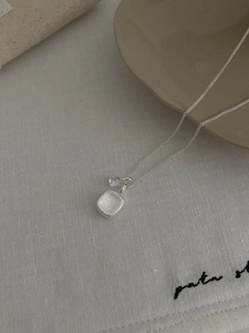 Macro detail of silver sugar-cube pendant with hammered texture and zircon on linen