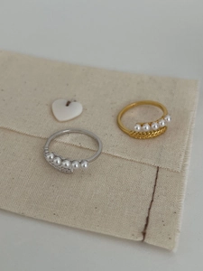 Dettaglio di anelli in argento s925 con cinque perle e trama a spiga di grano su tessuto