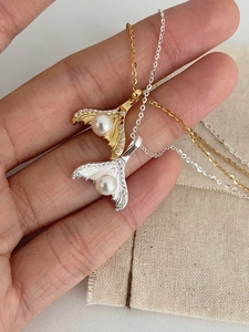 Detailed shot of silver and gold mermaid tail pendants with pearls and zircon crystals