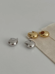 Close-up of polished gold and silver water drop earrings on a minimalist canvas background