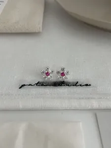 Close-up of sparkling five-petal flower stud earrings with a pink gemstone center