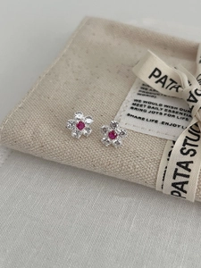 Macro detail of silver flower earrings featuring a red center stone and white petals