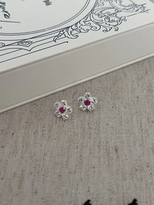 Macro shot of silver floral stud earrings with red crystal center and sparkling petals