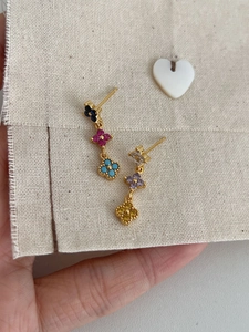 Détail de boucles d'oreilles trèfle à trois niveaux dorées avec strass colorés