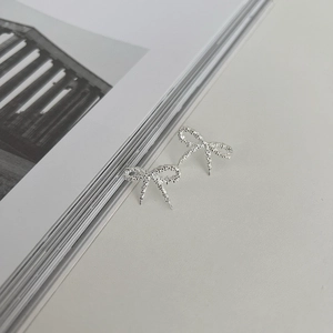 Macro shot of silver bow stud earrings with sparkling texture on a minimal book background