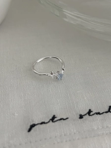 Macro shot of liquid texture silver ring featuring a square blue gemstone on white fabric