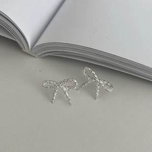 Minimalist S925 silver bow earrings with textured woven finish on a book background