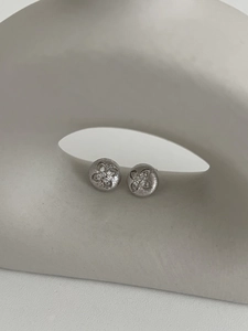 Close-up of brushed silver clover studs with pavé zircons on white geometric stand
