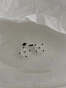 Macro detail of silver window-grille earrings with black zircon and geometric patterns