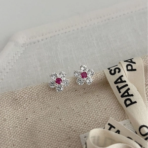 Elegant floral stud earrings with red and white zircons on a beige linen surface