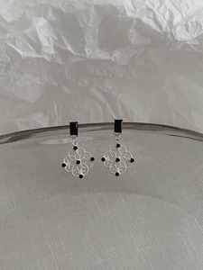 Macro detail of silver openwork window earrings featuring elegant black gemstones
