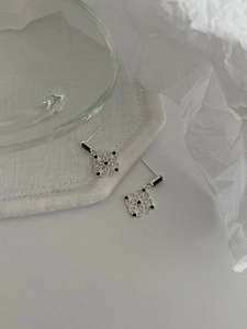 Close-up of silver hollow floral earrings with black pearl detail on neutral fabric