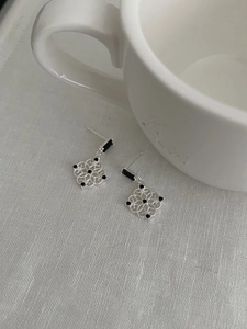 Detail of silver hollowed window earrings with black stones on textured fabric