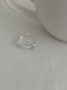 Detail of adjustable S925 silver ring with blue square gem and wavy band on white linen