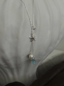 Detailed view of silver necklace with starfish, seashell pendants and white pearl charms