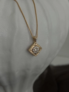 Detail of vintage gold necklace featuring a diamond-shaped hollow pendant with white gems
