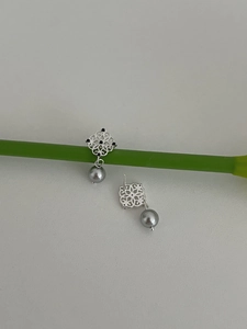 Detail of silver drop earrings with square hollow pattern and grey pearl charm on plant
