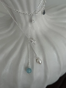 Detail of silver starfish necklace with white pearl and light blue bead on a white surface