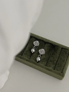Macro detail of silver hollow flower earrings with grey pearl in a green velvet box
