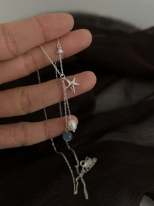 Detail of silver starfish pendant with white pearl and blue bead on a delicate chain