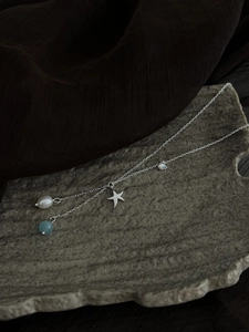 Close-up of ocean-themed necklace with starfish, shell charms and irregular pearl on stone