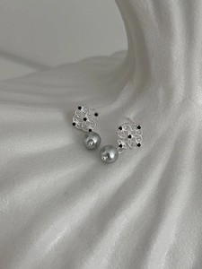 Detail of silver hollow floral earrings with grey pearls on elegant wavy white background