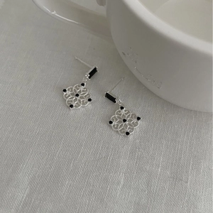 Silver hollow flower stud earrings with black gemstones on a white fabric surface