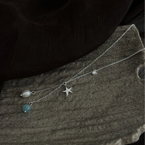 Starfish shell necklace with white pearl and blue bead on a grey stone display plate