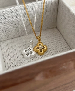 Dettaglio di pendenti a quadrifoglio in oro e argento con trama in metallo spazzolato e zircone