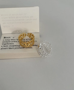 Close-up of gold and silver layered chain rings with heart charms on minimalist prop card