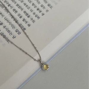 Collier chaîne à billes en argent avec pendentif gemme jaune et halo sur un livre