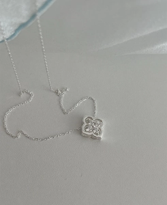 Detailed close-up of a silver four-leaf clover pendant with sparkling center stones on silk