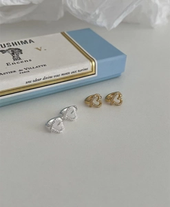 Macro detail of gold and silver heart-shaped earrings with zircon stones on gray background