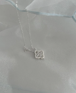 Detailed close-up of a silver four-leaf clover pendant with small zircons on blue silk