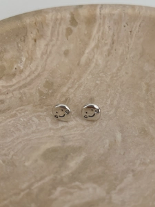 Dettaglio macro di orecchini a lobo smiley in argento S925 con trama metallo liquido