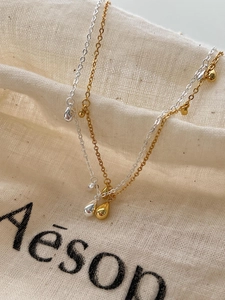 Macro shot of minimalist teardrop pendants in gold and silver finish on linen fabric