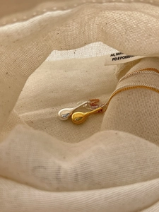 Macro detail of gold and silver teardrop pendants on a beige textured fabric bag