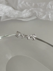 Détail de boucles d'oreilles nœud argenté avec texture striée sur un support en verre pur