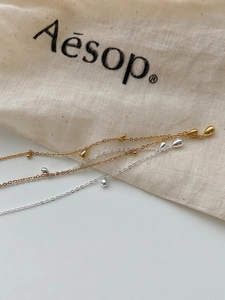 Close-up of minimalist gold and silver teardrop pendant necklaces on a linen bag