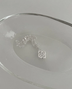 Macro shot of silver four-leaf flower pendant with crystals on a glass tray
