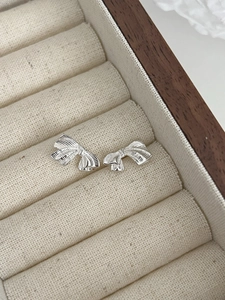 Détail de boucles d'oreilles nœud argenté avec texture brossée sur présentoir en lin