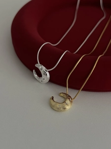 Detail of silver and gold crescent moon necklaces with brushed texture on red velvet