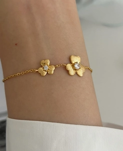 Macro detail of a gold clover bracelet with matte textured petals and sparkling stones