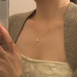 Detailed close-up of a minimalist gold pearl necklace and matching ring on a model