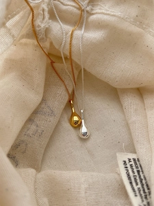Close-up of polished gold and silver teardrop pendants on textured fabric