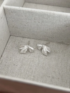 Gros plan de boucles d'oreilles nœuds argentés avec texture striée dans un écrin beige