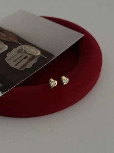 Détail de boucles d'oreilles cœur dorées avec zircons sur un support en velours